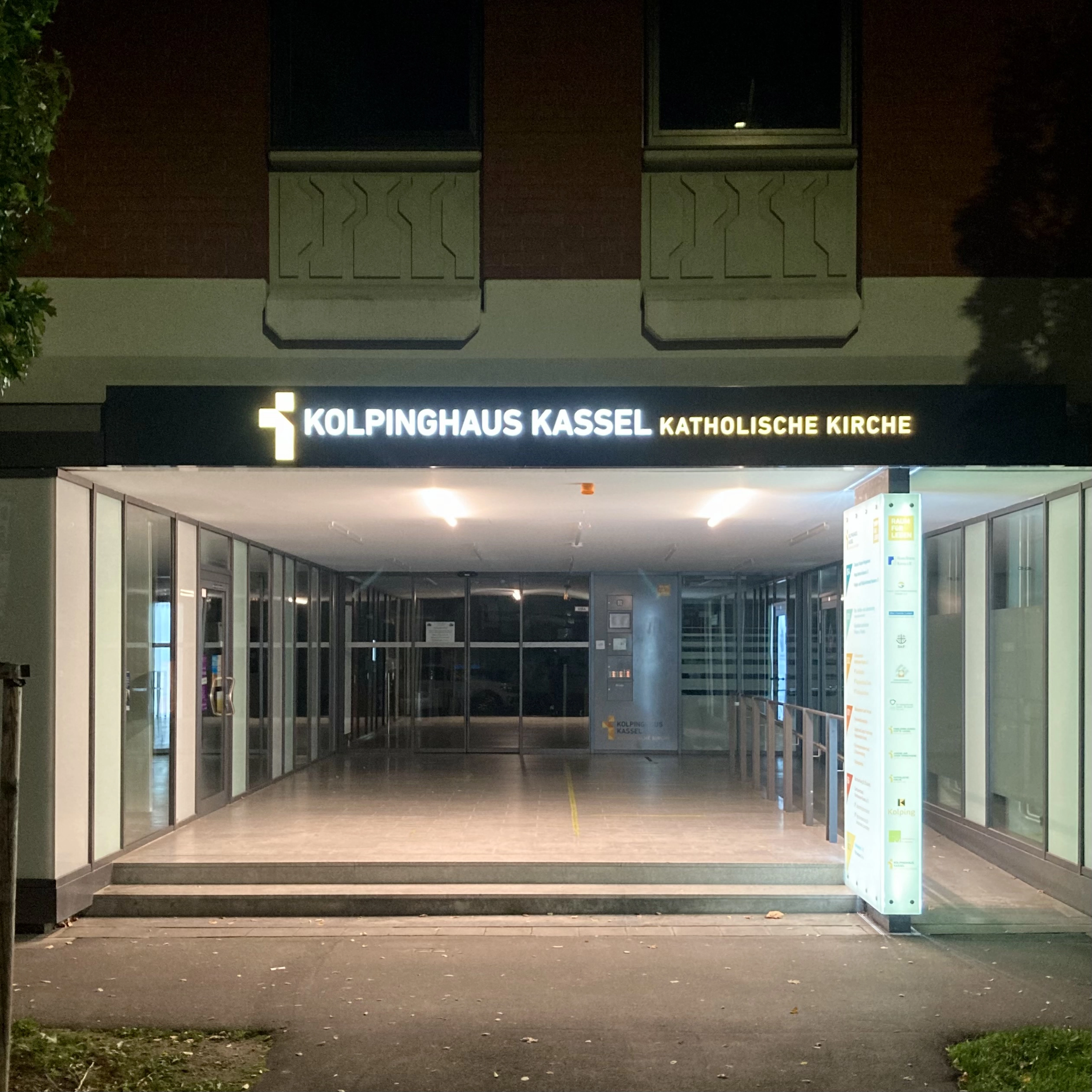 Eingang Frontal fotografiert mit leuchtendem Logo im Dunkeln.